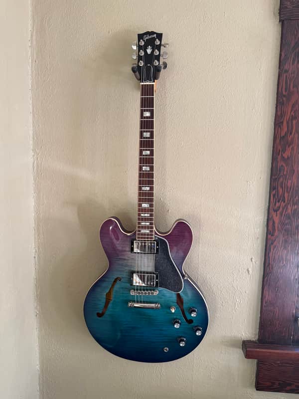 Blue electric guitar with black pickguard, visible neck, and hardware.