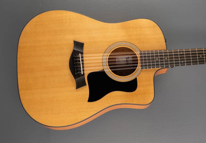 A natural wood acoustic guitar with a black pickguard, shown against a gray background.