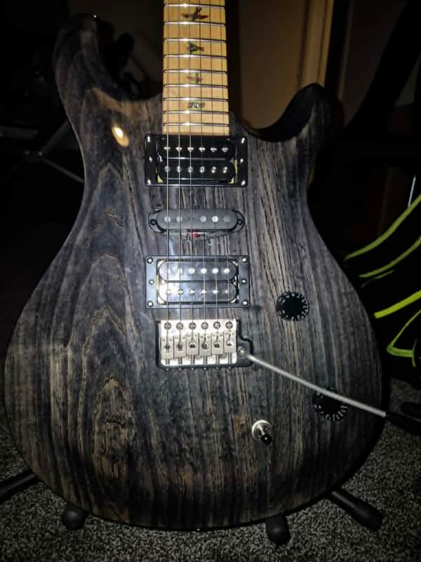 Orange and brown electric guitar body with black strap, resting on black case.