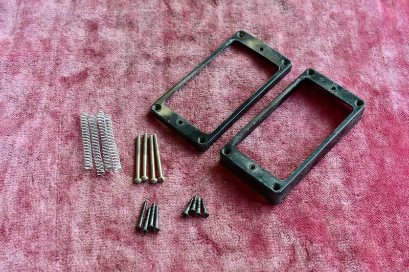 Two black metal picture frames and assorted silver screws on pink fabric.