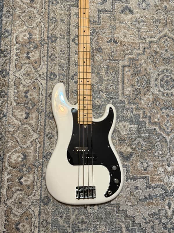 Black electric guitar on stand, wooden neck, against white door.