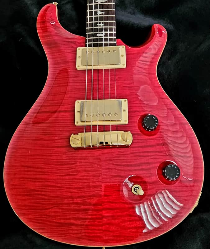 Orange electric guitar with black pickguard, visible wood grain, resting on patterned rug.