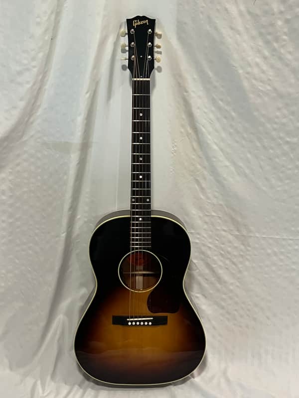 A natural wood acoustic guitar with a red inlay, displayed outdoors on wood.