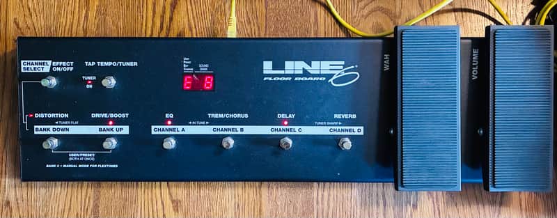 Black guitar effects pedal with multiple knobs and switches on wooden surface.