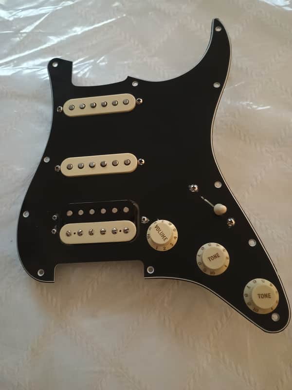White Fender guitar pickguard with circular logo in center.