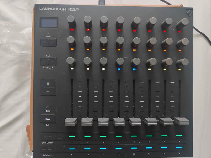 Grey electronic control panel with numerous buttons and sliders in cardboard box.